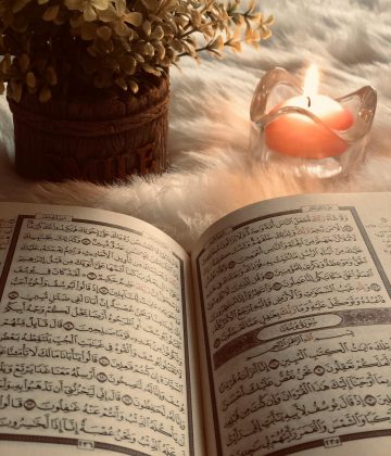 A Quran open to Surah An-Nur, with candlelight ambiance and decorative flowers.