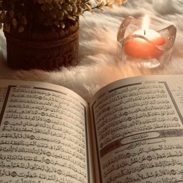 A Quran open to Surah An-Nur, with candlelight ambiance and decorative flowers.